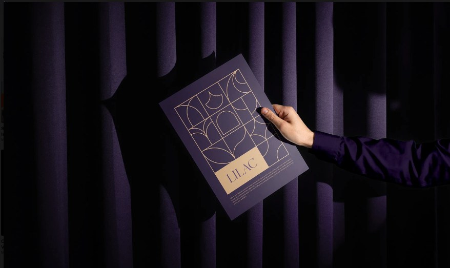 Mão segurando pôster roxo com padrão geométrico dourado da marca Lilac